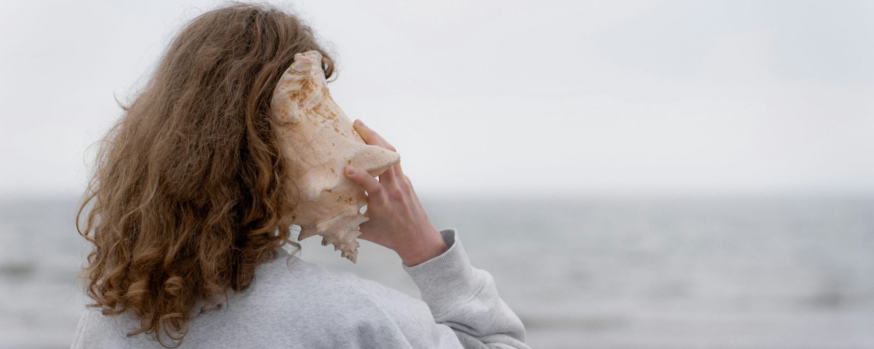 A girl holding a large seashell to her ear